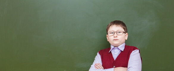 boy standing with his arms crossed at a school board. in glasses and school uniform