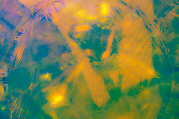 A vibrant, abstract artwork featuring a close-up of a shiny, surface reflecting multicolored light. The dominant hues are red, orange, yellow, and pink, with hints of blue and green.