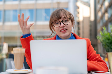 Young woman discussing ideas while working on a laptop at a modern outdoor cafe in an urban setting...