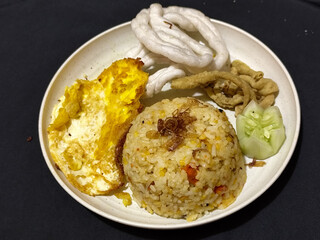Fried rice served with sunny side up egg and fresh cucumber slices on a white plate, looks very delicious.