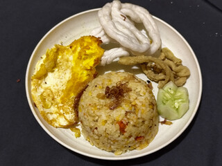Fried rice served with sunny side up egg and fresh cucumber slices on a white plate, looks very delicious.