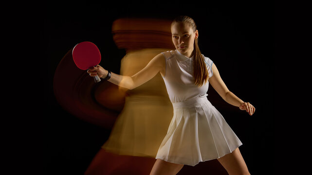 Focused female table tennis player with blurred motion behind on black background. Concept of dynamic movement, training intensity, agility with emotional determination.