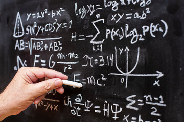 Mano escribiendo operaciones y formulas de física cuántica y matemáticas con una tiza en la...
