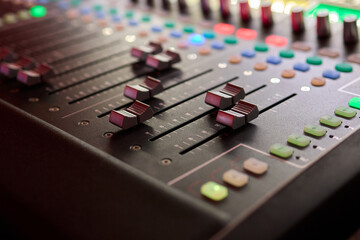 Closeup image of a hand mixing sounds on a control board, showcasing an audio technicians work