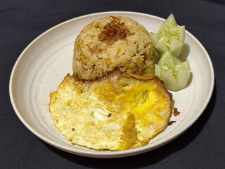 Fried rice served with sunny side up egg and fresh cucumber slices on a white plate, looks very delicious.