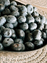 Fresh blueberries piled in a silver bowl on a woven placemat during afternoon light