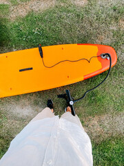 Person standing on grass next to an orange paddleboard with a paddle in hand