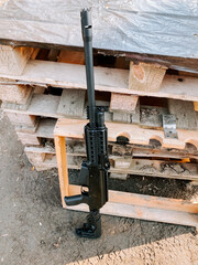 Firearm resting on wooden pallets in an outdoor environment during daylight