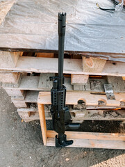 Black rifle resting against wooden pallets in outdoor environment during daylight