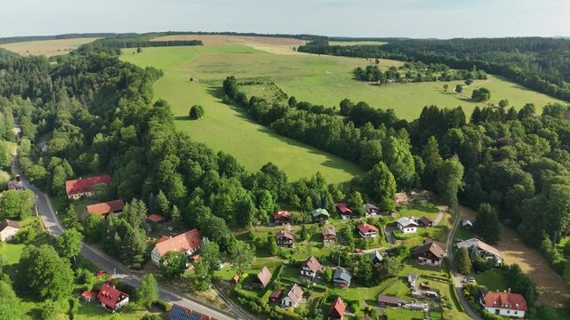 Aerial view of green hills, dense forests, scattered cottages, and winding roads near Teplice Rocks in Adrspach-Teplice Mountain Park, Bohemia, Czech Republic &ndash; peaceful summer landscape