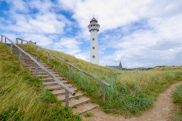 The J.C.J. van Speijk Lighthouse tower with european marram grass (beach grass) under blue sky in summer, Dutch north sea coastline, Egmond aan Zee, Municipality of Bergen, Noord Holland, Netherlands.