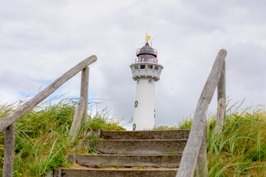 The J.C.J. van Speijk Lighthouse tower with european marram grass (beach grass) under blue sky in summer, Dutch north sea coastline, Egmond aan Zee, Municipality of Bergen, Noord Holland, Netherlands.