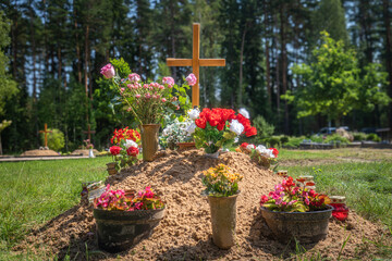 Fresh Grave with Colorful Flowers and Wooden Cross in Rural Cemetery – Symbol of Mourning, Faith and Hope. Christian Burial Tradition