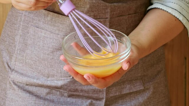 Female hands beating eggs with a whisk in a bowl to prepare dough for muffins and cookies