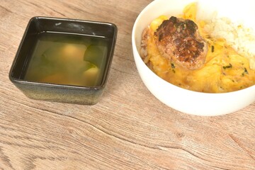 grilled hamburg pork steak and creamy egg omelets topping on rice in bowl with miso or soy sauce soup