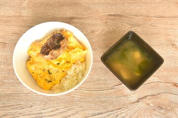 grilled hamburg pork steak and creamy egg omelets topping on rice in bowl with miso or soy sauce soup