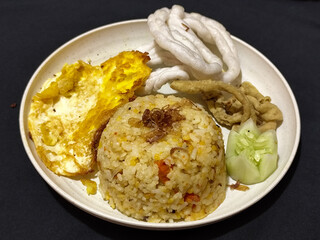 Fried rice served with sunny side up egg and fresh cucumber slices on a white plate, looks very delicious.