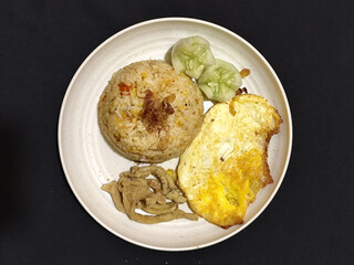 Fried rice served with sunny side up egg and fresh cucumber slices on a white plate, looks very delicious.