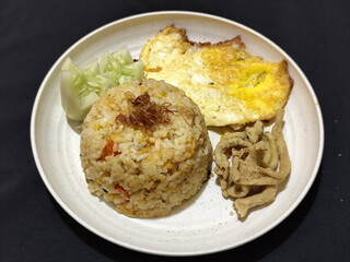 Fried rice served with sunny side up egg and fresh cucumber slices on a white plate, looks very delicious.