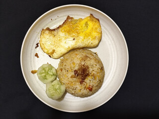 Fried rice served with sunny side up egg and fresh cucumber slices on a white plate, looks very delicious.