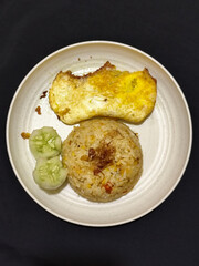 Fried rice served with sunny side up egg and fresh cucumber slices on a white plate, looks very delicious.