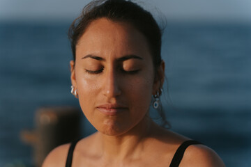 Young woman meditating with closed eyes by the sea at sunset