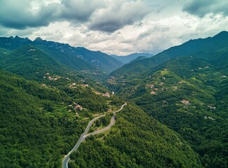 Beautiful, winding asphalt road in the green forest with mountains and clouds in the background, northern Italy. A scenic highway for car travel through the natural landscape of the Alps. Restaurant C
