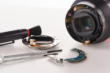 A broken lens of a professional camera and repair tools on a white table.