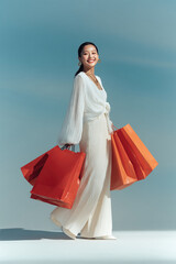 fashionable chinese asian woman in white outfit smiles while holding bright orange shopping bags. Her joyful and stylish attire create vibrant fun shopping scene