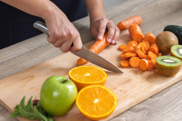 Hands of a woman cutting some vegetables and fruits in wooden table in the kitchen