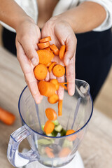 Hands of young woman making a vegetable smoothie in the kitchen at home.