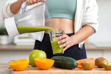 Influencer woman serving detox juice into glass while listening music in the kitchen.