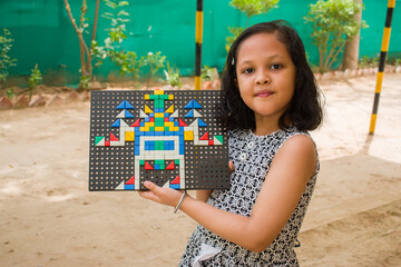 A little girl smiling and showing pegboard mosaic in which she arranged colorful geometric shaped...
