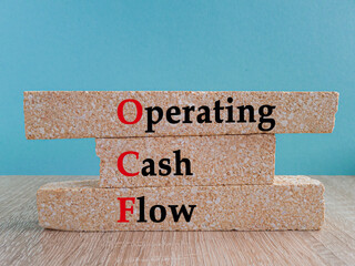 Brick blocks with the acronym OCF-operating cash flow. Beautiful blue background, wooden table....