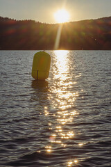 Bright yellow buoy floating on calm lake water at sunset. Golden reflections on surface. Vertical...