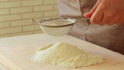 Female hands sifting flour on a wooden board to prepare dough - Powered by Adobe