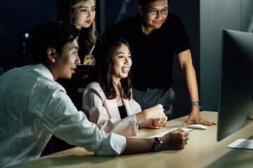 Group of Southeast Asian colleagues working together at night in modern office, illuminated by computer light, showcasing teamwork, innovation, and positive energy. 