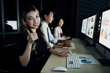 Smiling female team member showing approval gesture while monitoring financial analytics with colleagues. Represents success in technology-driven financial operations.