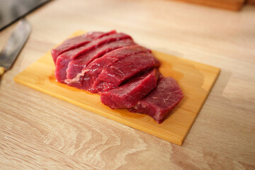 A piece of fresh beef is placed on a wooden cutting board in a bright kitchen.