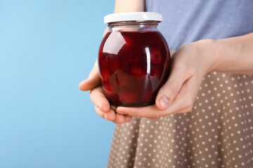 Woman with tasty cherry jam on light blue background, closeup