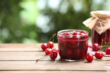 Tasty cherry jam and fresh fruits on wooden table against blurred background, closeup. Space for text