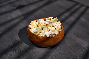 Freshly popped popcorn served in a wooden bowl with shadows creating an artistic effect on a textured surface