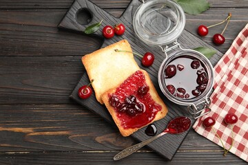 Toasts with tasty cherry jam and fresh fruits on black wooden table, flat lay
