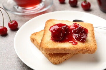 Toasts with tasty cherry jam, tea and fresh fruits on grey table , closeup