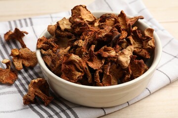 Dried chanterelle mushrooms in bowl on light wooden table, closeup