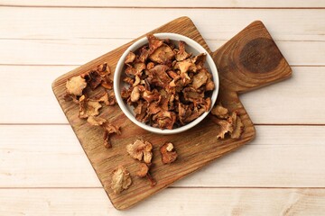Dried chanterelle mushrooms in bowl on light wooden table, top view