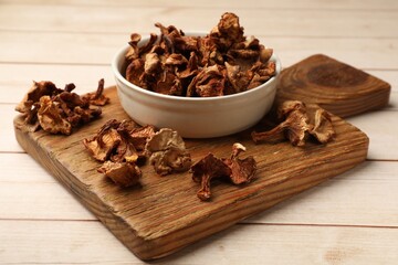 Dried chanterelle mushrooms in bowl on light wooden table, closeup
