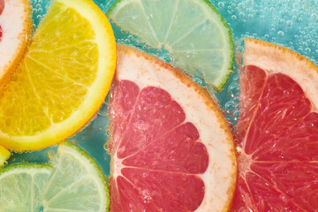 Slices of grapefruit, lemon, and lime float in sparkling water, showcasing bright colors and bubbles