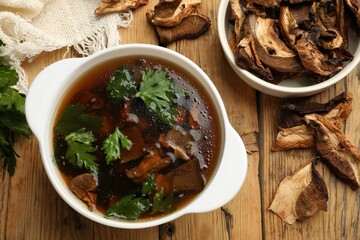 Tasty soup with mushrooms and parsley in bowl on wooden table, flat lay