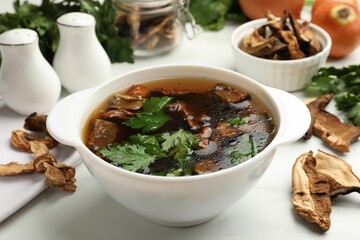 Tasty soup with mushrooms and parsley in bowl on white table, closeup
